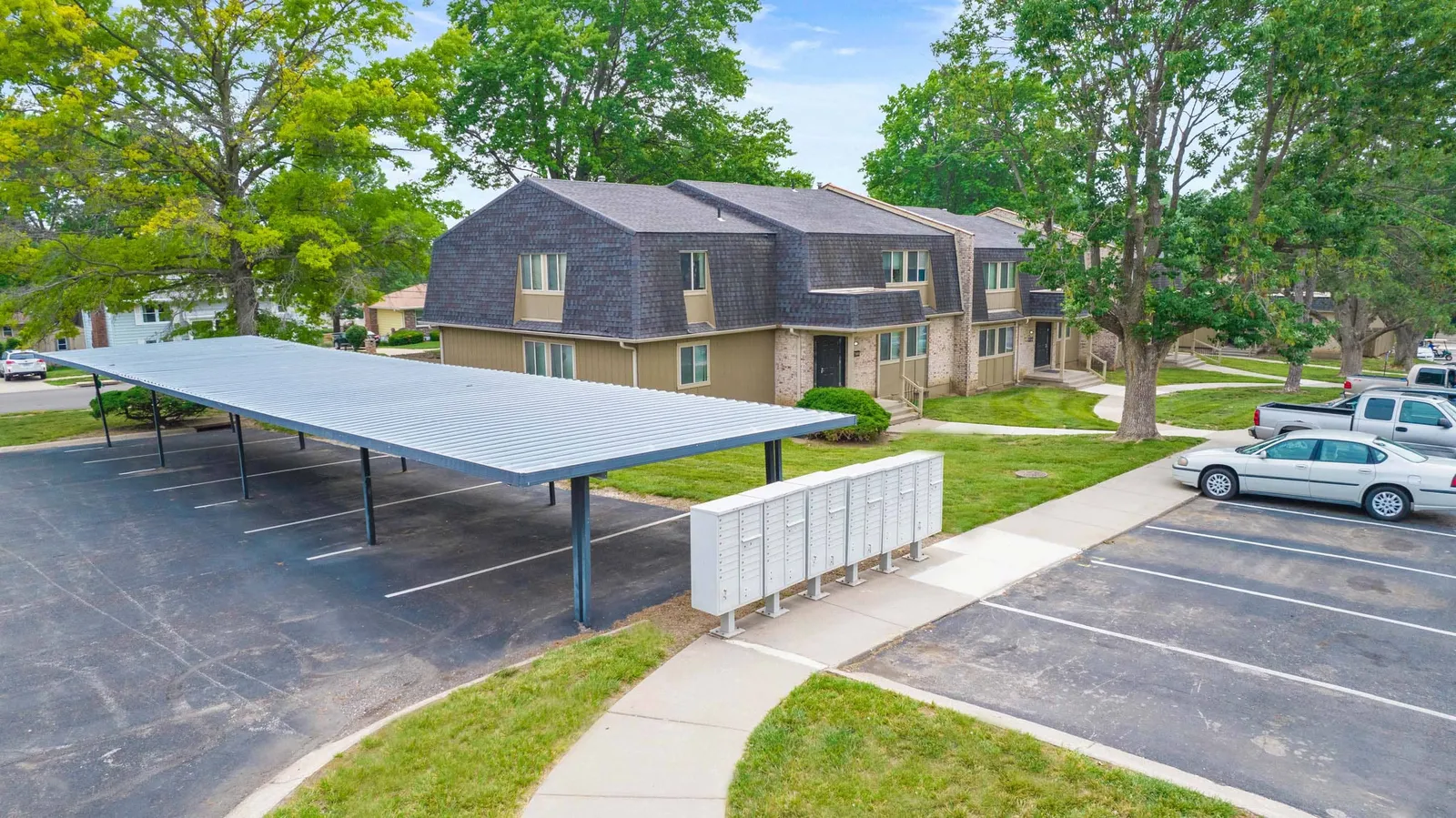 The Oaks at Prairie View - a parking lot with covered parking, mail boxes, and trees